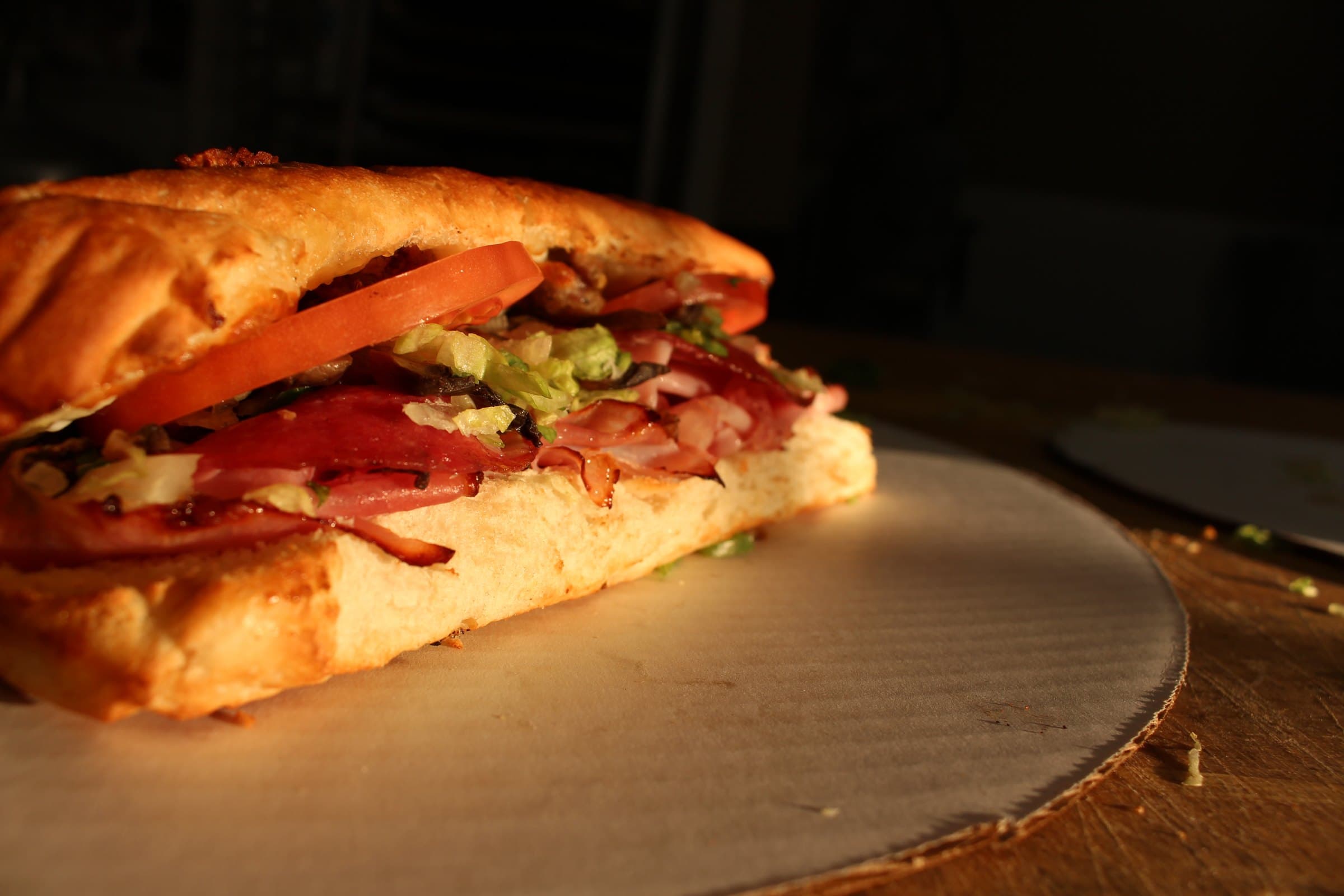A hot grinder on fresh-baked bread, piled with sliced meats, lettuce, and tomato.
